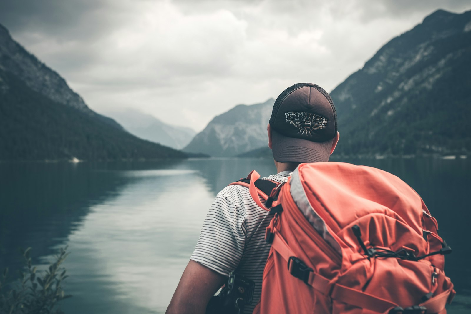 Viajante de costas contempla lago entre montanhas